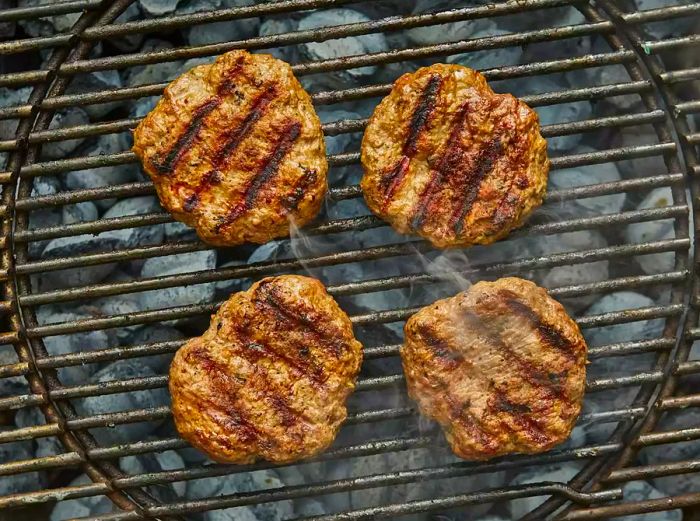 A top-down view of four lamb patties grilling on a barbecue.