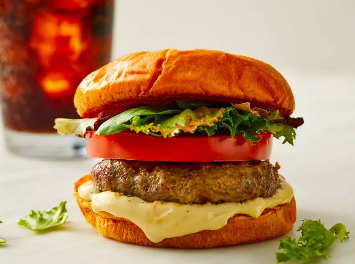 A lamb burger served on a plate, with a soda in the background.