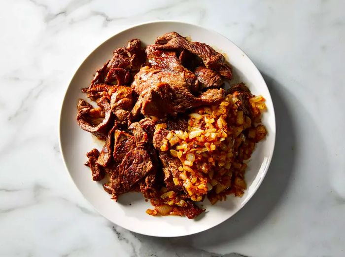 A top-down image of cooked beef, onions, and garlic arranged on a white plate.
