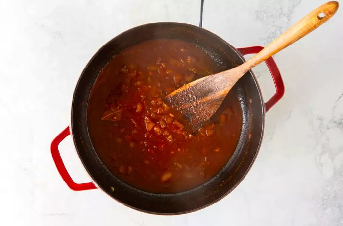 Beef broth being poured into the pot with cooked shallots.