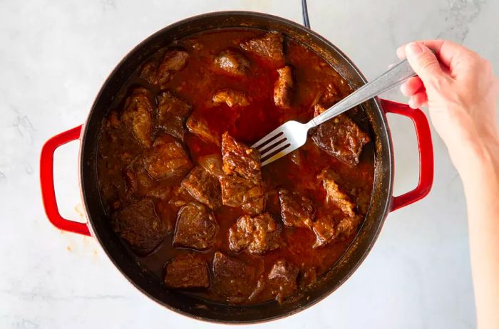 A person checking the doneness of the beef in the pot.