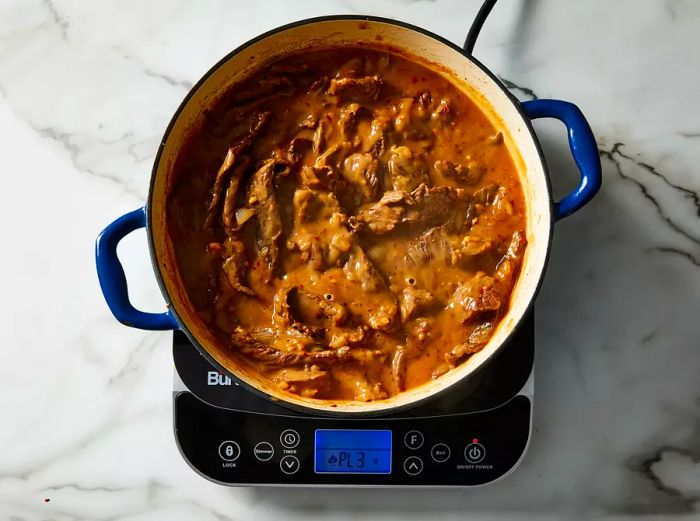 A top-down image of beef, onions, and garlic added to the simmering stock in the pot.