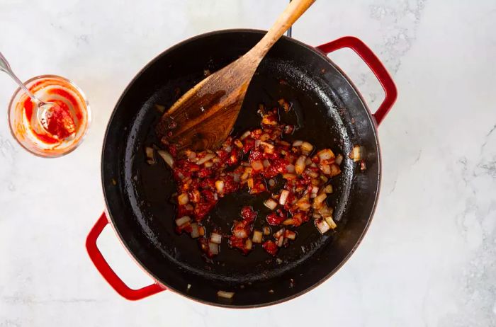 Onion, garlic, and tomato paste cooking together in an enameled cast iron skillet.