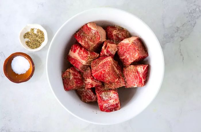 Chunks of beef, seasoned with salt and pepper, resting in a white bowl.