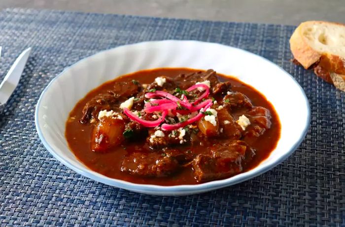 A white bowl filled with Greek-style beef stew and shallots