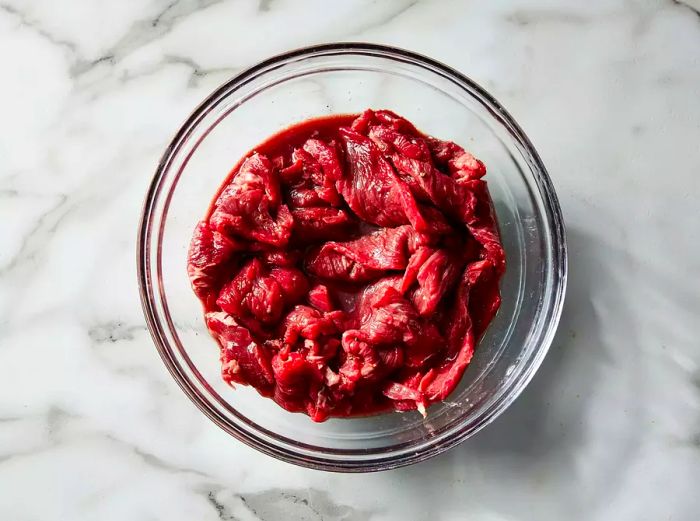 A top-down view of beef soaking in a mixture of red wine, salt, and black pepper in a bowl.