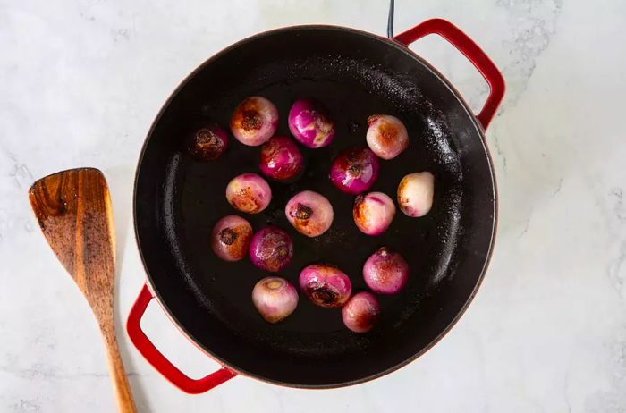 Peeled shallots sautéing in an enameled cast iron skillet.