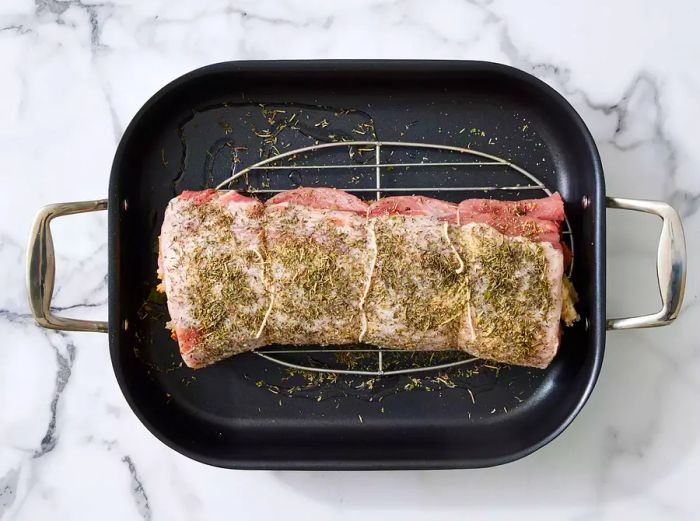 A stuffed pork loin, topped with a sprinkle of herbs, resting in a roasting pan