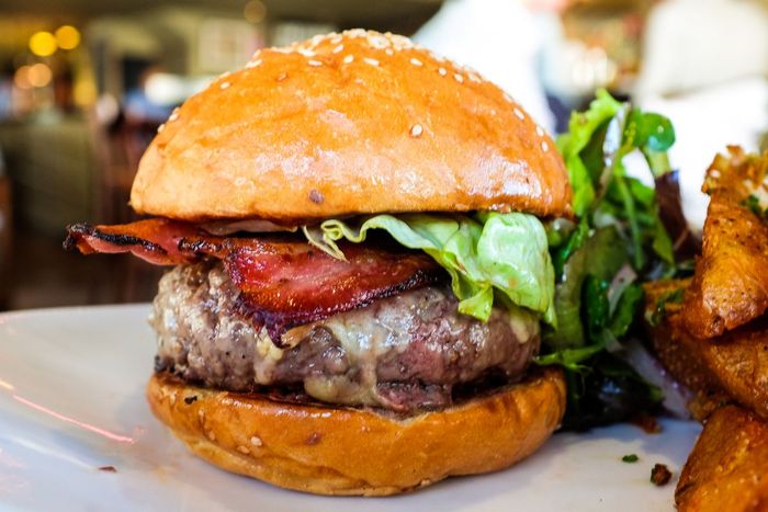 Cận cảnh một chiếc bánh burger phô mai dày, phủ thịt xông khói và rau diếp, kèm theo khoai tây chiên dày.