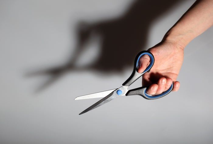 A pair of scissors held in a hand casts a rabbit-shaped shadow on the wall