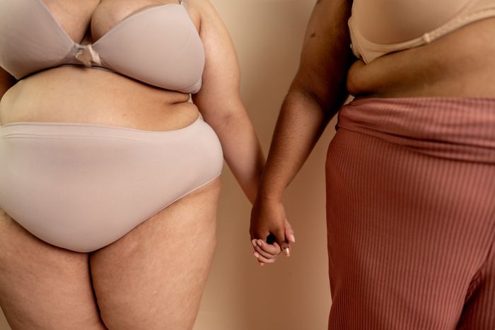 Two people holding hands, one in underwear and the other in a skirt and bra, promoting body positivity and self-acceptance