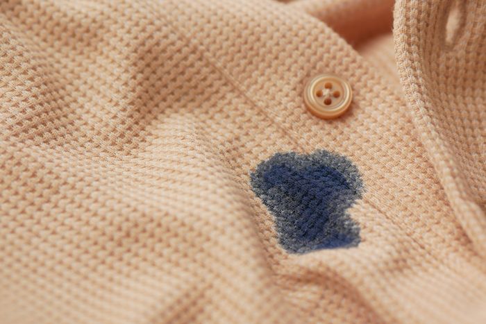 A close-up view of textured fabric with a button, featuring a dark ink stain near the center