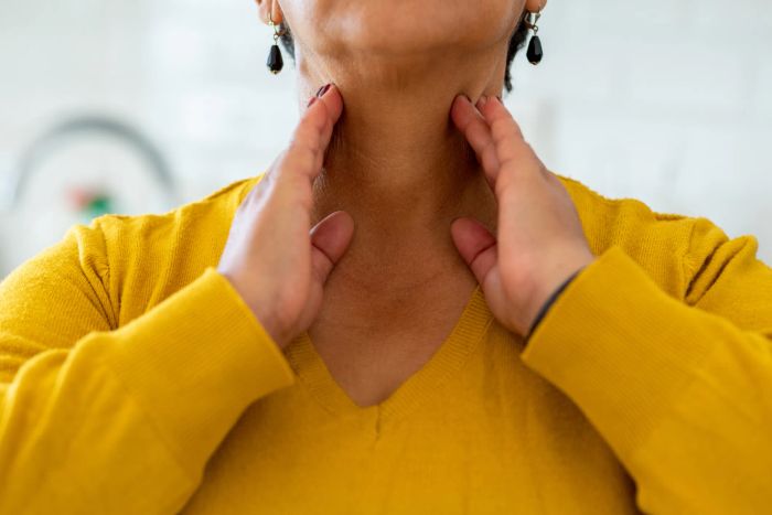 A person is gently touching their neck with both hands while wearing a V-neck sweater and earrings.
