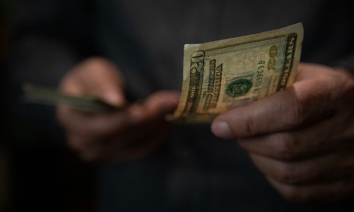 A person holds and counts several twenty-dollar bills