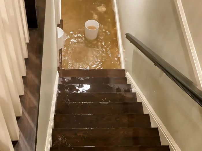Waterlogged basement stairs with water accumulating at the bottom; two buckets placed to catch the water