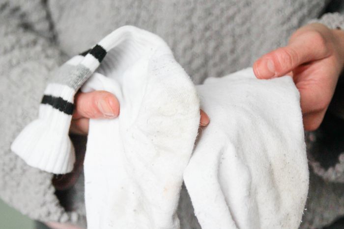 A person holds two socks, one with black stripes, both showing signs of wear
