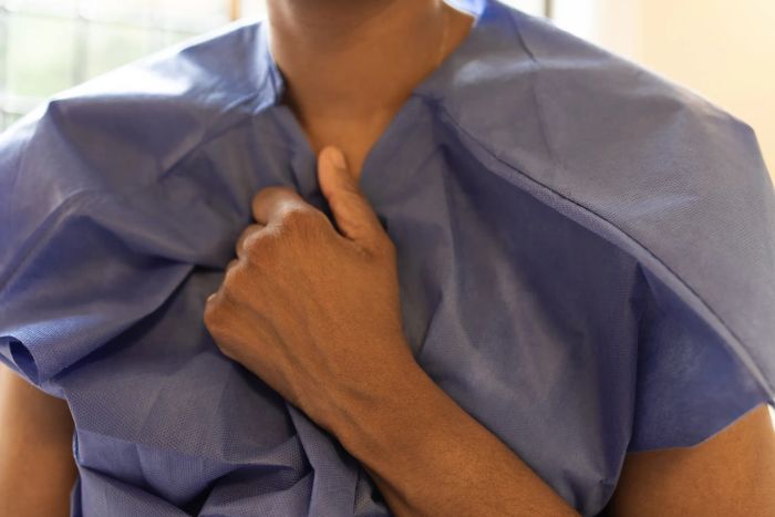 A person in a medical gown, holding it closed with one hand