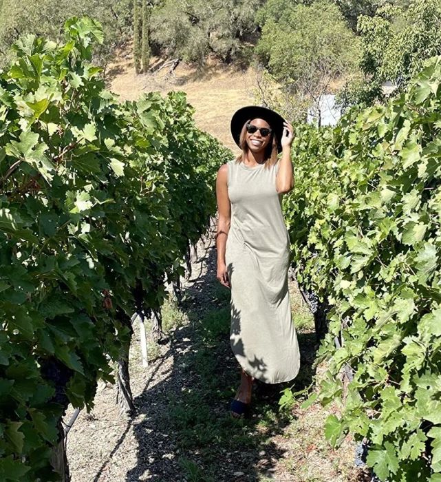 A reviewer stands in a vineyard, wearing a light green dress paired with a sunhat.