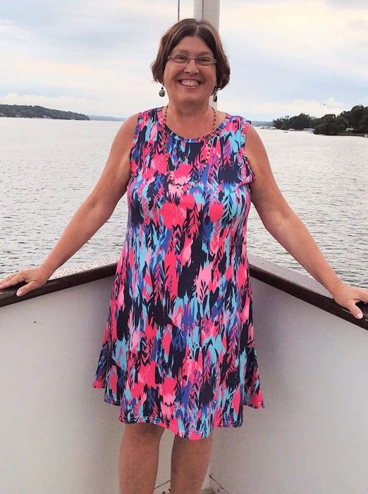 A reviewer wearing a pink and purple feather print dress.