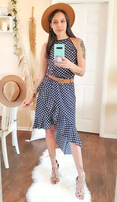A woman in a polka-dot crop top outfit and a hat snaps a mirror selfie