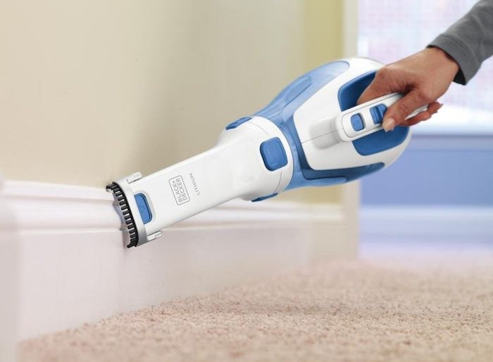 model cleaning a baseboard with a handheld vacuum featuring a long, narrow attachment