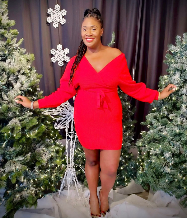Reviewer in a stylish red off-shoulder dress stands between festively decorated trees with snowflakes