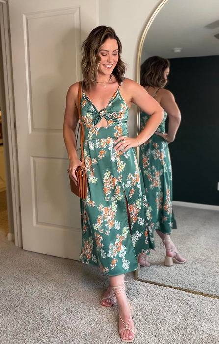 Person smiling in a mirrored room wearing a floral dress with cutouts and strappy sandals