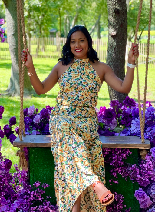 Reviewer in a floral dress sitting on a swing surrounded by artificial purple flowers