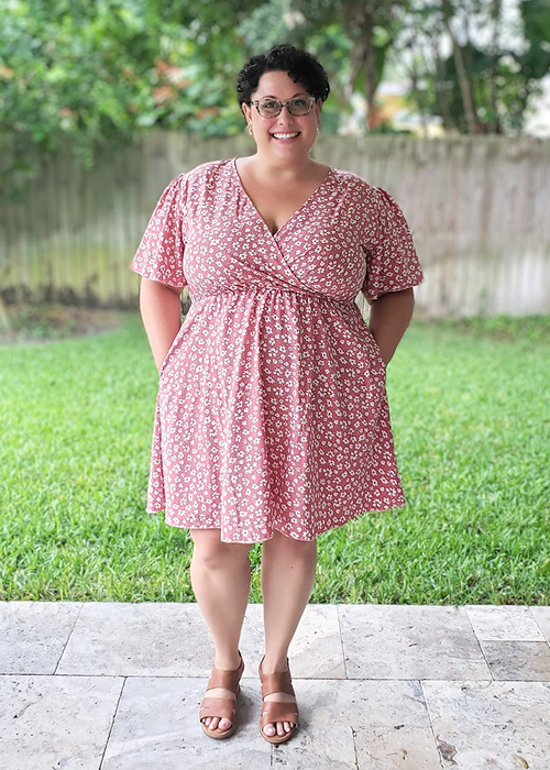 reviewer in a knee-length dress with a colorful floral print and white short sleeves, featuring a V-neck