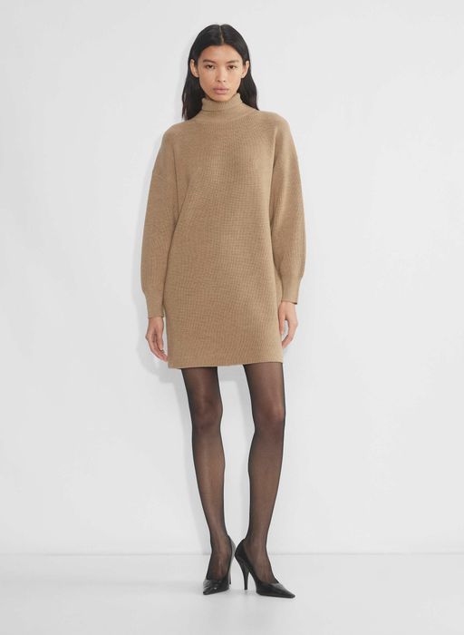 A model showcases a chic knee-length sweater dress in khaki, paired with sheer tights and elegant heels, perfect for a sophisticated autumn look.