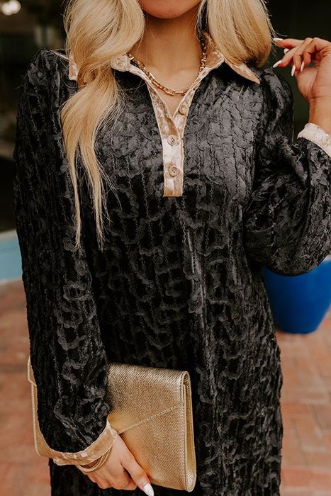 A person models a black textured dress adorned with gold accents, paired with a metallic clutch, creating a sophisticated and trendy look perfect for a shopping feature.