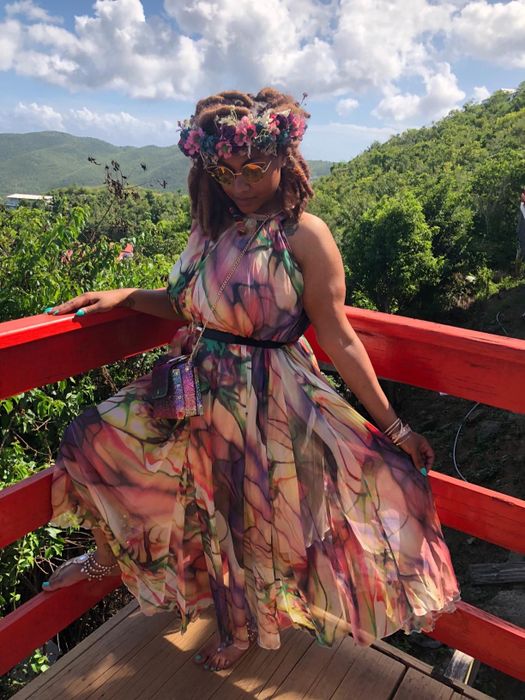 reviewer in a floral dress and headpiece sitting on a red bridge railing outdoors