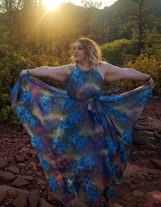reviewer in a flowing floral dress posing in nature at sunset