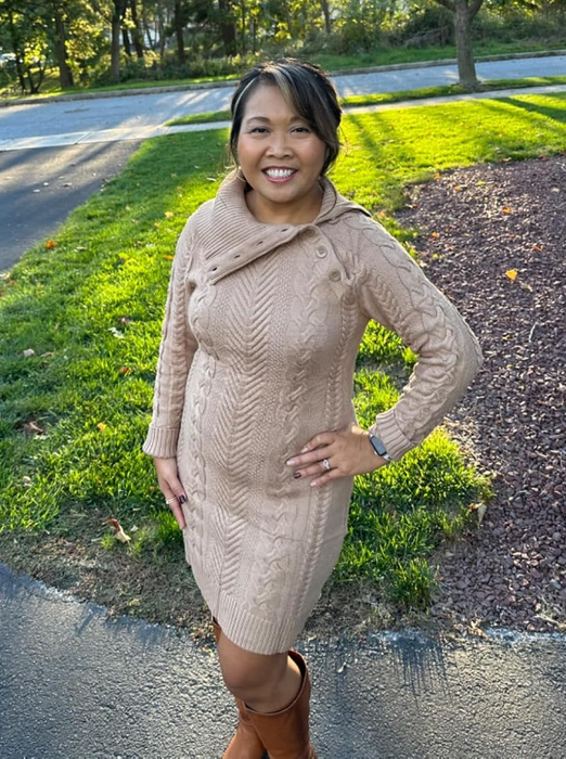A person outdoors, wearing a warm apricot knit sweater dress paired with knee-high boots, smiles confidently at the camera