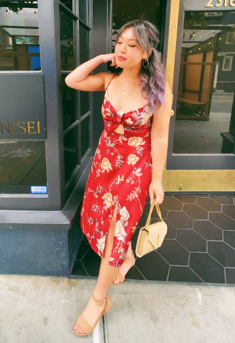 Woman in a floral dress with a slit, holding a purse, standing by a restaurant entrance