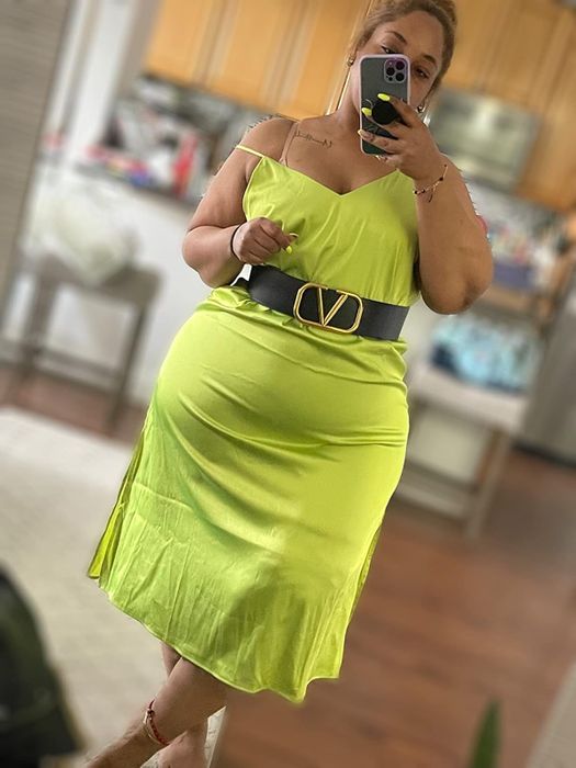 A person takes a mirror selfie in a stylish green slip dress, accessorized with a designer belt, showcasing a chic and casual look perfect for a shopping feature