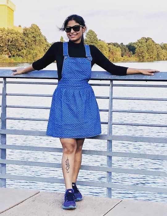 A reviewer wearing the above-the-knee, flared, polka dot, blue denim pinafore
