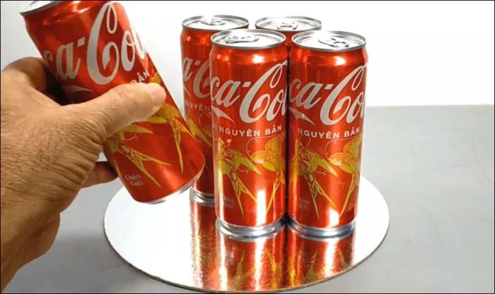 Sắp xếp 5 lon Coca lên tấm bìa carton hình tròn và dùng keo nến để cố định chúng.