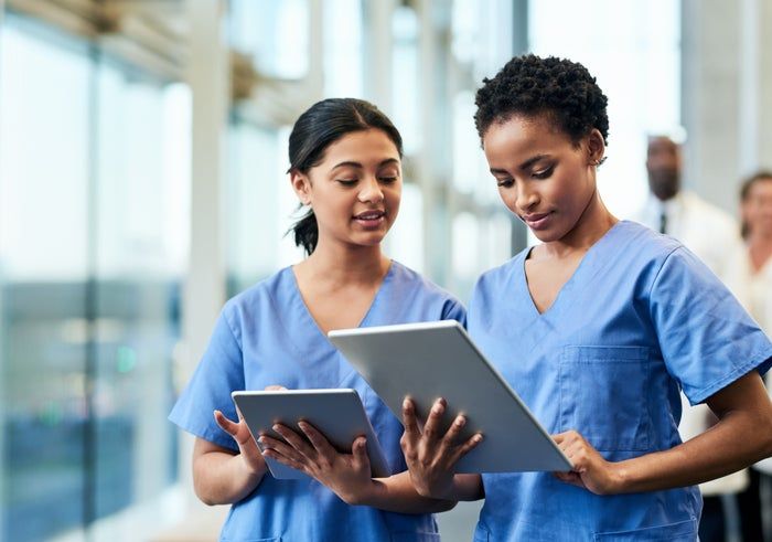 Two medical professionals dressed in scrubs assess data on tablets in a bright, modern environment