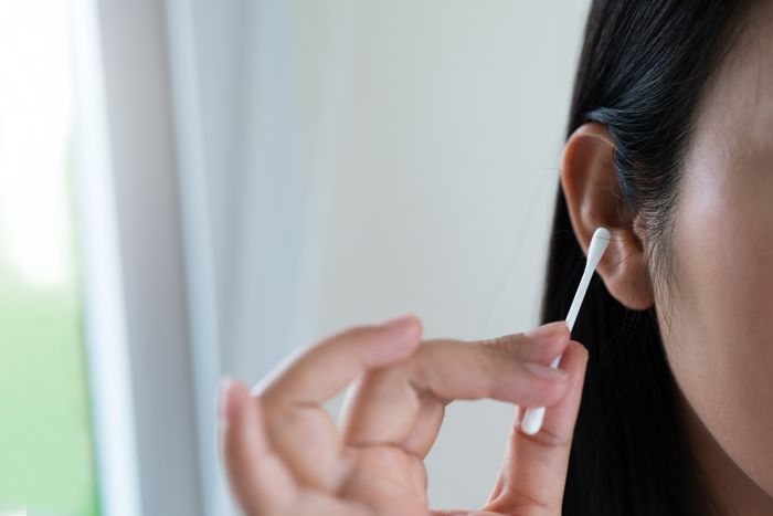 A person using a cotton swab to clean their ear, with a close-up of the ear and hand