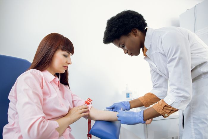 A healthcare provider taking a blood sample from a seated patient in a clinical environment.