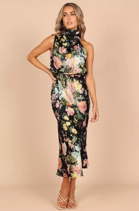 Model wearing a floral print sleeveless dress and strappy heels strikes a pose against a simple background.