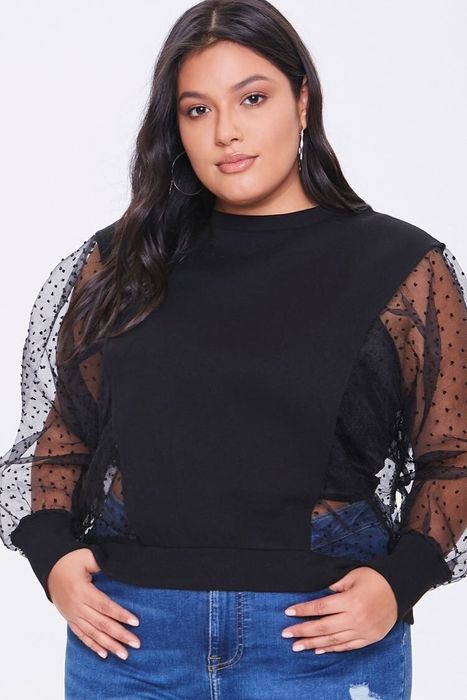 A model is styled in a black balloon sleeve top with mesh dot sleeves, paired with blue jeans