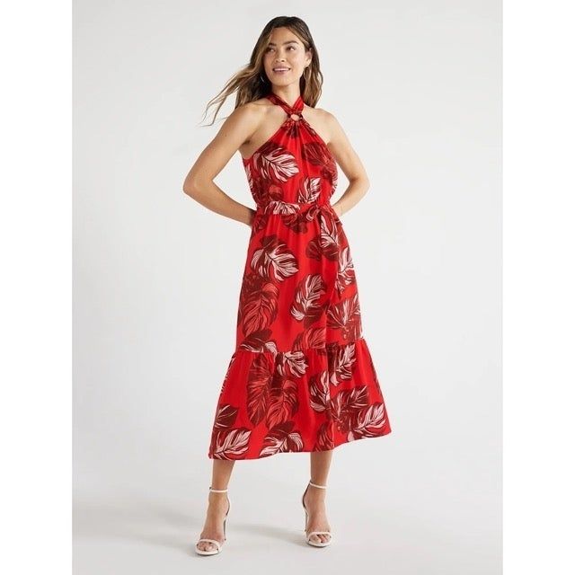 A model is showcasing a halter neck dress featuring a vibrant red leaf pattern.