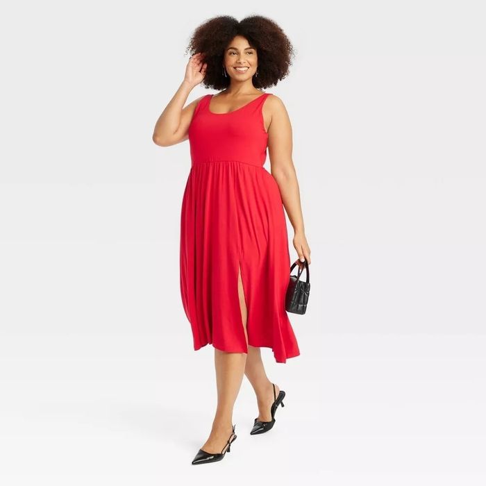 The model wears a sleeveless red dress with a side slit, paired with a small black handbag and black flats.