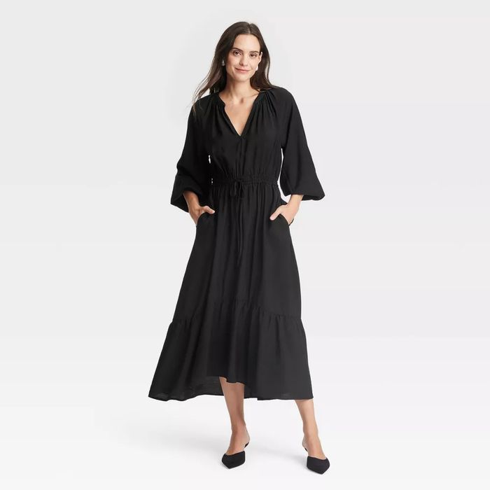 A model confidently strikes a pose in a long, flowing black dress with pockets.