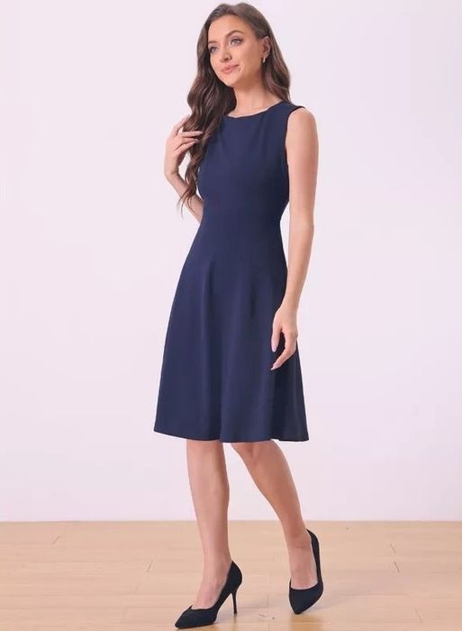 A person models a sleeveless, knee-length dress with a fitted bodice and flared skirt, paired with heels.