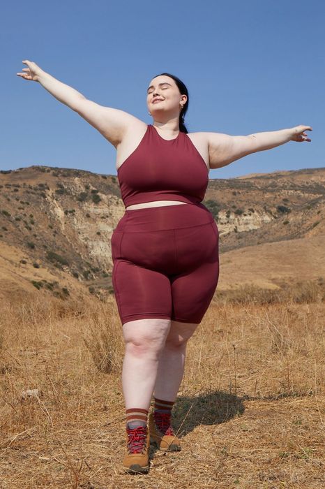 A model is styled in high-rise dark red bike shorts, a matching sports bra, and brown hiking boots