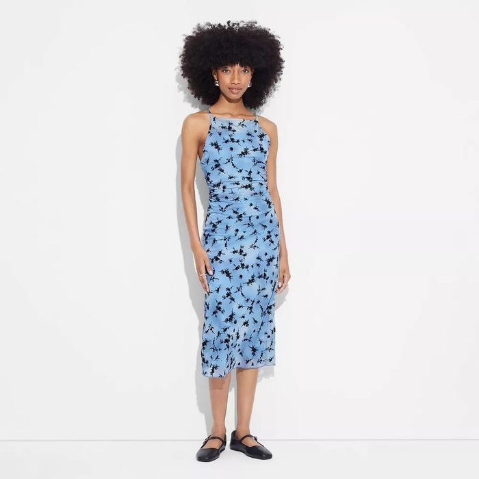 The model is dressed in a knee-length floral patterned sleeveless dress.