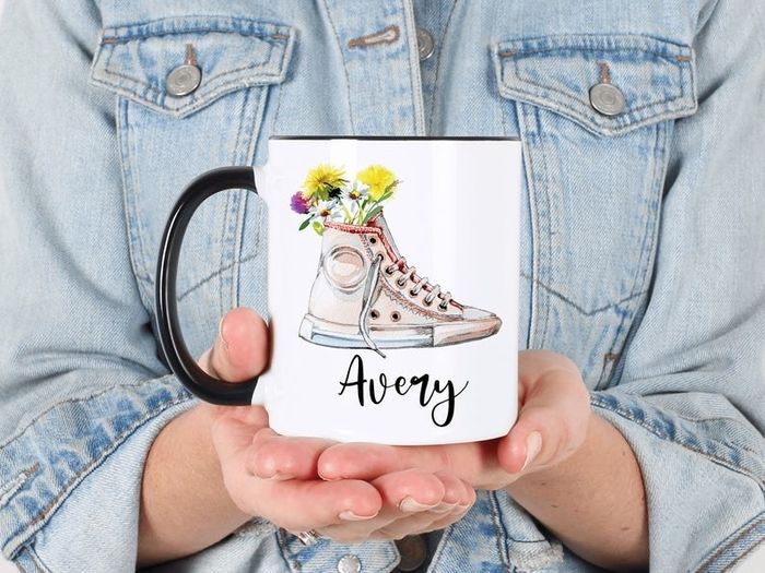 A model holding the mug featuring a Converse sneaker filled with flowers and a name written in black cursive